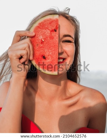 Happy smiling young woman with slice of watermelon half hiding face. Vacation photography. Royalty-Free Stock Photo #2104652576