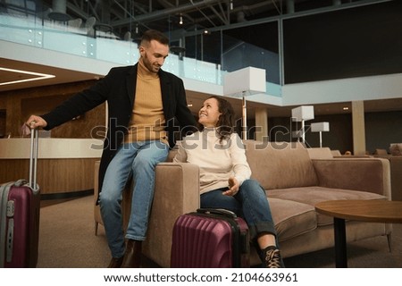 Woman and man in casual clothes with suitcases sitting on armchair in the international airport terminal lounge, looking at each other, discussing forthcoming flight, waiting for airplane departure Royalty-Free Stock Photo #2104663961