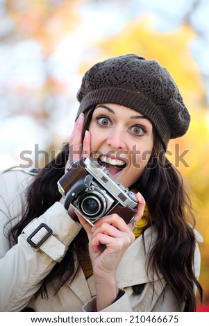 Fashionable surprised woman taking photos with retro film camera in autumn season. Amazed expressive photographer enjoying and having fun. Fashion girl wearing warm clothes.