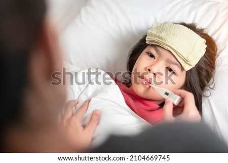 Asian mother measuring temperature girl with digital thermometer in her mouth on bed at morning time, Sick child have cool towel for reduce high fever,  Selective focus, Healthy and infection concept Royalty-Free Stock Photo #2104669745