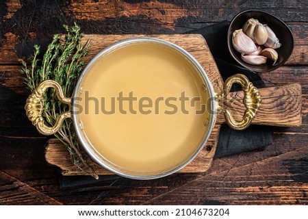 Clear broth stock without meat in cooking skillet. Wooden background. Top view