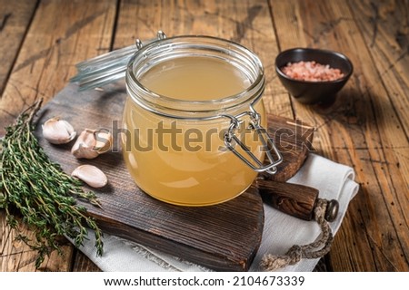 Bone broth for chicken soup in a glass jar. Wooden background. Top view