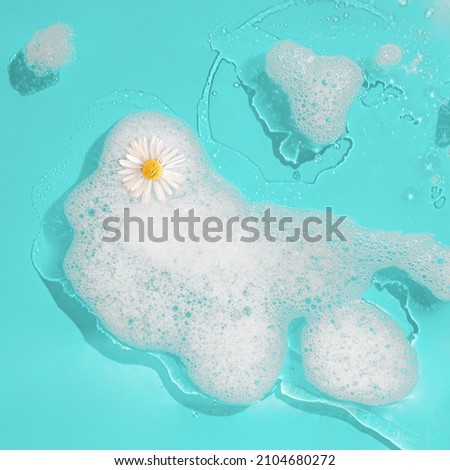 Minimal aesthetic abstract scene with white daisy flower standing on the foam on a wet turquoise background. Holistic lifestyle. Luxury wellness concept. Flat lay. Relaxing bath card. Top view. Royalty-Free Stock Photo #2104680272