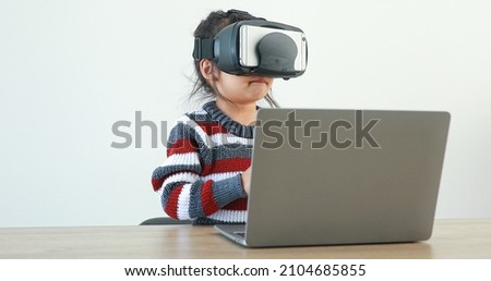 The little girl wearing VR sitting at desk in the home glasses virtual Global Internet connection metaverse. Future kids in white clothing wearing VR headsets for a game. concept advanced technology. 