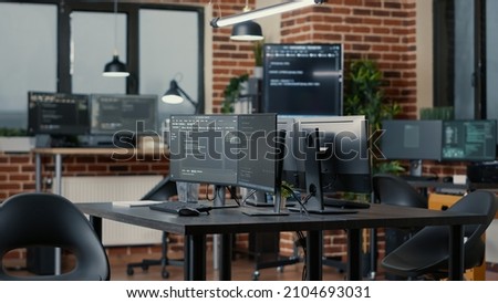 Computer screens running programming code in empty software developing agency office and computers parsing data algorithms in background. Neural network servers cloud computing in data room. Royalty-Free Stock Photo #2104693031