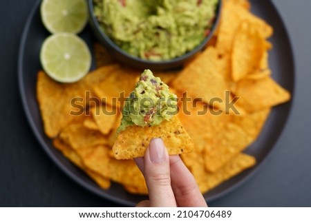 Top view of woman hand holding tortilla chips or nachos with tasty guacamole dip Royalty-Free Stock Photo #2104706489