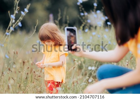
Mother Taking a Picture of her Daughter Playing in Nature. Mommy recording memories with her smartphone 

