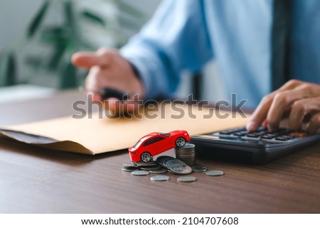  Toy car on stack coins and man holding the key car in hand. after completes the insurance policy or rental documents. Car insurance concept Royalty-Free Stock Photo #2104707608