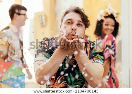 Brazilian Carnival. Young man enjoying the carnival party blowing confetti Royalty-Free Stock Photo #2104708145
