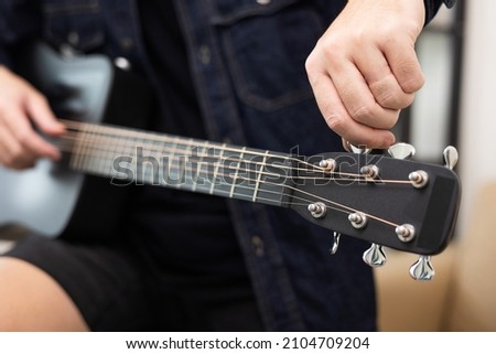 Close up man tuning guitar in living room at home. Relaxing with song and music. Man having fun playing acoustic guitar Royalty-Free Stock Photo #2104709204