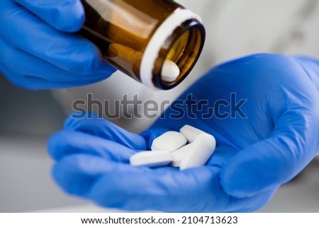 Closeup of medical worker or pharmacist hands wearing blue latex protective gloves,pouring white medicine pills on palm of hand,Coronavirus therapy treatment illustration,cure for COVID-19 new variant Royalty-Free Stock Photo #2104713623