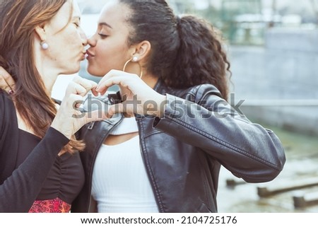 Happy mother and daughter portrait.
African Teenage girl and her caucasian mother kissing and making heart shape with hands.