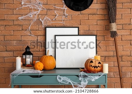 Blank frames with Halloween decor on table near brick wall