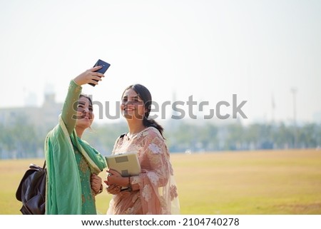 South Asian tourists backpackers taking selfie with smartphone while traveling on holidays in Wat Phra Kaew or Emerald Buddha Temple a tourist landmark in Bangkok Thailand