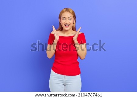 Beautiful young Asian woman in red dress showing cheerful and excited face over purple background