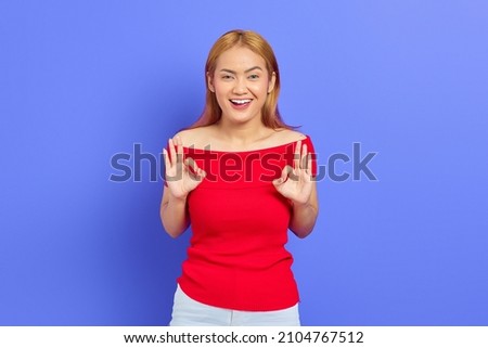 Portrait of a smiling positive Asian woman posing making okay gesture isolated on purple background