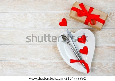 valentines day table setting flat lay with love white ceramic plate shape heart, festive decoration, fork and knife and red eco friendly zero waste gift box copy space text.
