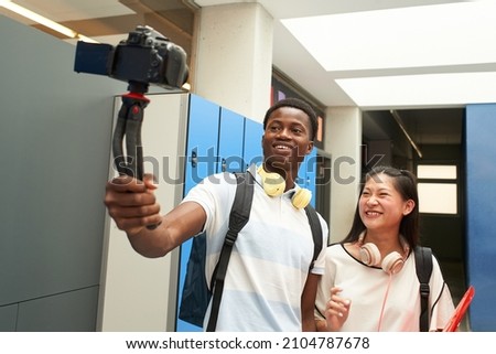 Interracial student couple making a video for social media. Selfie of two young people taking selfie in high school with a video camera. Vlogging.
