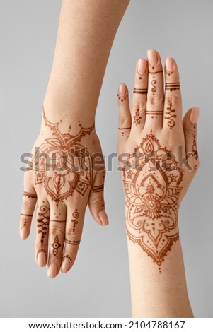 Beautiful female hands with henna tattoo on grey background Royalty-Free Stock Photo #2104788167