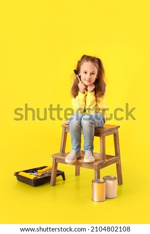 Cute little girl with paint brush on yellow background