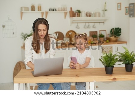 Work from home. A tired woman sits at a computer while a child sits on the phone and watches cartoons or videos.