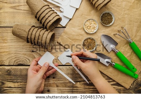 Top view of seeds and garden tools on a wooden background. Growing seedlings using peat cups. The concept of spring gardening at home. Women's hands sign a sign for the plant.