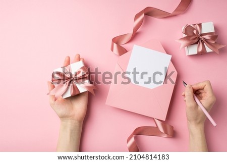 First person top view photo of st valentine's day decor female hands holding pen pink envelope with letter small giftbox and pink silk curly ribbon on isolated pastel pink background with empty space Royalty-Free Stock Photo #2104814183