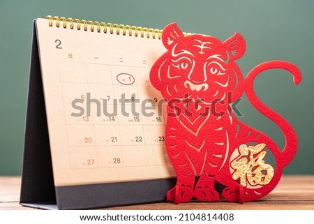Chinese New Year of Tiger mascot paper cut and a 2022 calendar with the New Year day highlighted, the Chinese means Happy New Year no logo no trademark Royalty-Free Stock Photo #2104814408