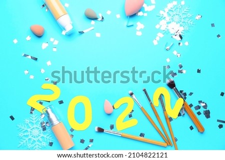 Frame made of makeup supplies and figure 2022 on color background