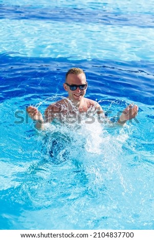 Young attractive man in sunglasses is resting in the pool on summer vacation. The guy in the pool by the hotel