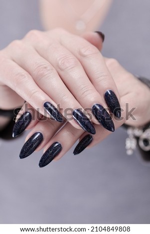 Female hands with long nails and dark black manicure holding a bottle of nail polish