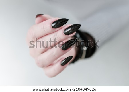 Female hands with long nails and dark black manicure holding a bottle of nail polish