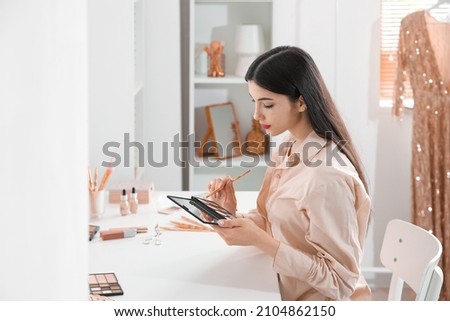 Beautiful young woman with brush and eyeshadows palette in dressing room