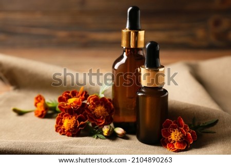 Bottles of essential oil and marigold flowers on wooden background
