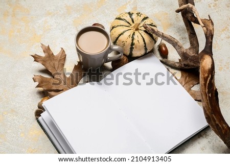 Cup of tasty coffee, blank book and autumn decor on light background