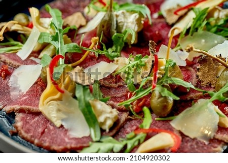 Beef carpaccio with capers, parmesan and truffle in a black plate. Selective focus, close-up. Noise grain in post-production