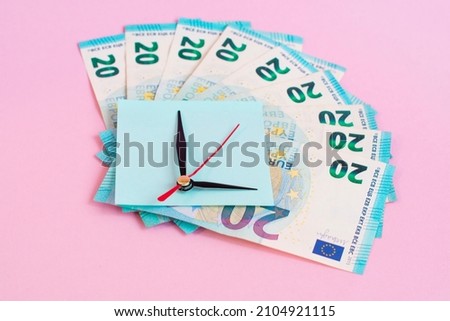 Clock hands on top of Euro banknotes on a pink background.