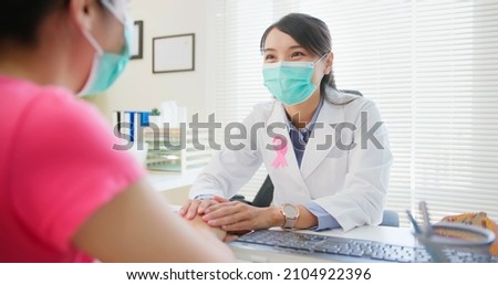 asian woman wears face mask to prevent COVID19 has breast cancer diagnosis in hospital - female doctor consulting to patient in patience and putting hand on her Royalty-Free Stock Photo #2104922396
