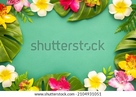 Summer background with tropical orchid flowers and green tropical palm leaves on green background. Flat lay, top view. Summer party backdrop