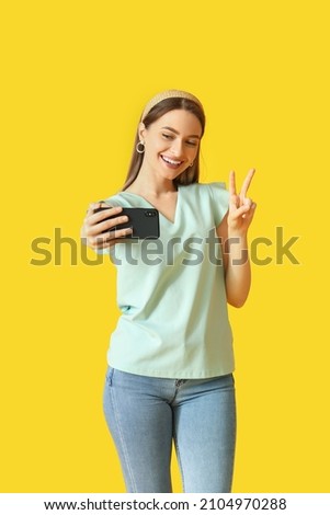 Pretty young woman taking selfie on color background