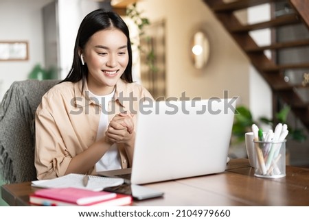 Asian girl studies at home using laptop computer. Young woman attends online classes, webinar or video conference, working on pc from home Royalty-Free Stock Photo #2104979660