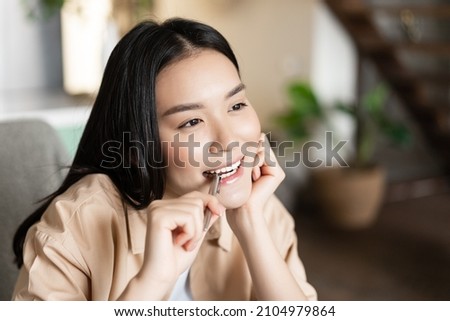Portrait of thoughtful asian girl biting pen and smiling, thinking, searching inspiration, doing homework and getting creative