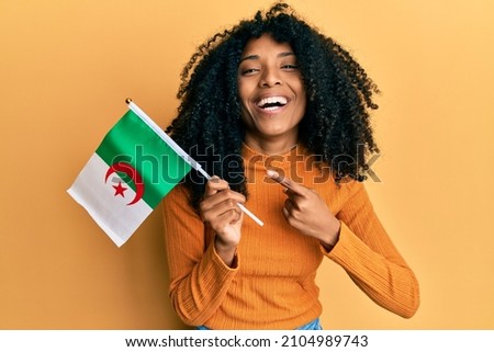 African american woman with afro hair holding algeria flag smiling happy pointing with hand and finger 
