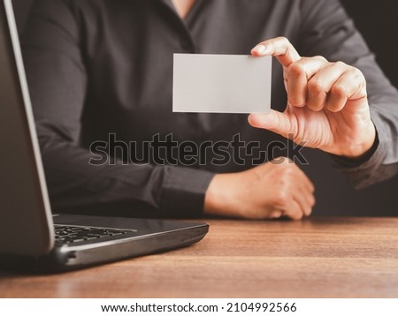 Close-up of hand a businessman in a black shirt holding a name card mockup while sitting in the office. Close-up photo. Business branding concept