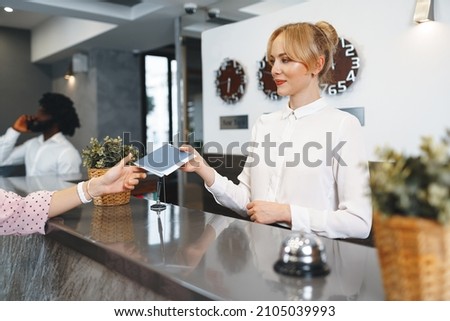 Hotel receptionist woman takes guest's passport for check in Royalty-Free Stock Photo #2105039993