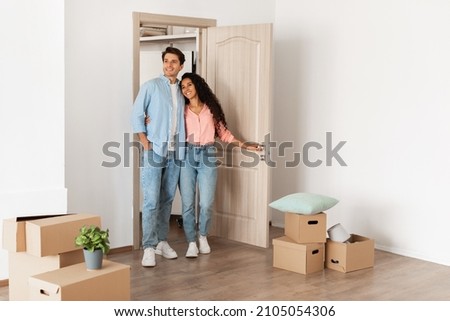Housing Concept. Happy couple walking in empty house with cardboard carton boxes on floor, young family moving into new apartment after buying house, excited guy and lady hugging, looking around flat Royalty-Free Stock Photo #2105054306