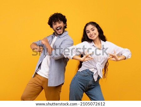 Having fun. Joyful young indian couple dancing and fooling around, enjoying favorite national music together on yellow studio background