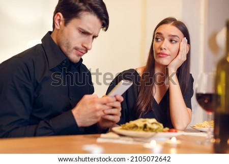 Bad Date. Unhappy Sad Beautiful Woman Is Getting Bored Sitting On Date Event In Restaurant While Her Boyfriend Using Mobile Phone And Chatting, Ignoring His Girlfriend. Relationship Problem Concept Royalty-Free Stock Photo #2105072642