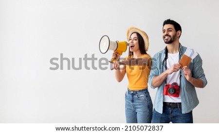 Young travellers couple with megaphone announcing excited deals for tourists, woman holding loudspeaker and pointing at free space, man holding passports and tickets, light background, panorama Royalty-Free Stock Photo #2105072837