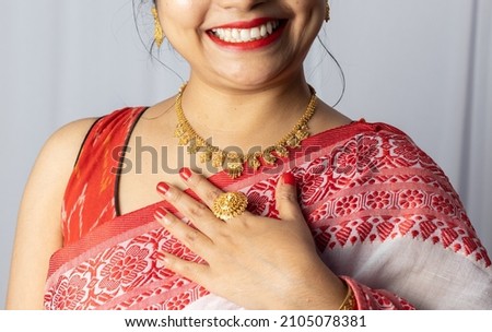 Close up of an Indian woman in red saree wearing gold ornaments with smiling face on white background